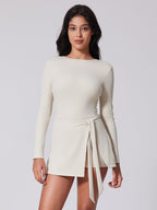 Woman wearing a white long-sleeve dress with a tie waist on a plain background