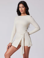Woman wearing a cream-colored long-sleeve dress with a front tie on a light gray background